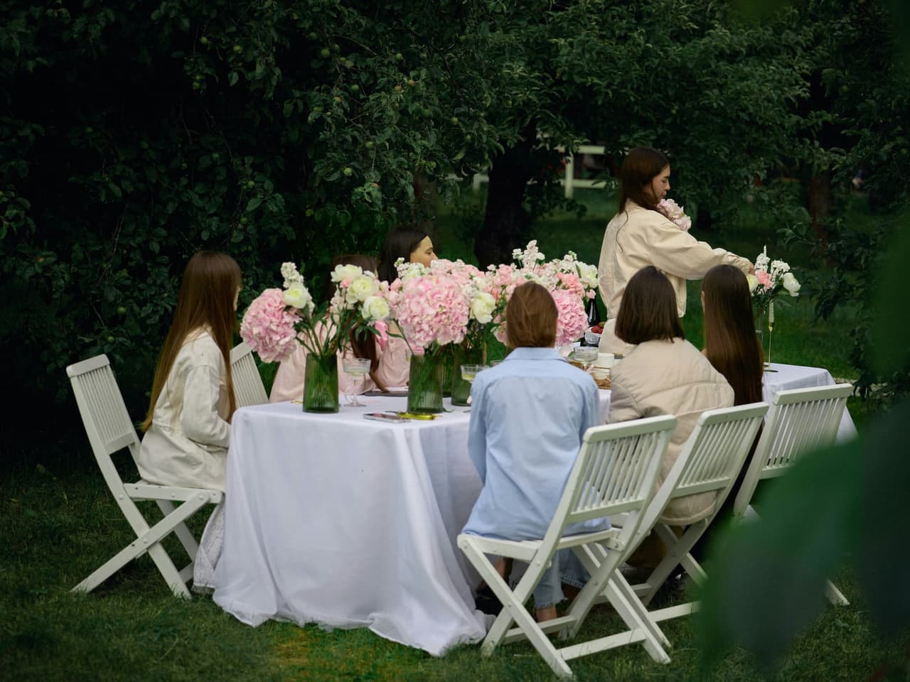 Table dressée sous les arbres pour une réception de mariage, bouquets et vaisselle blanche